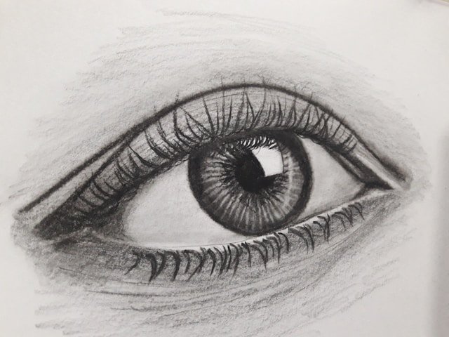 Realistic pencil drawing of a human eye on paper, featuring detailed shading.